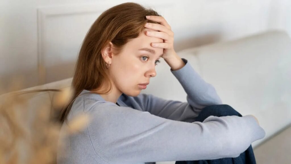 Young woman sitting with hand on forehead, looking anxious and distressed — a sign of an anxiety disorder